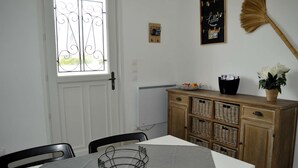 Un comedor con una mesa blanca, sillas, una cesta, un armario con cestas, una escoba y una ventana con detalles de hierro forjado.