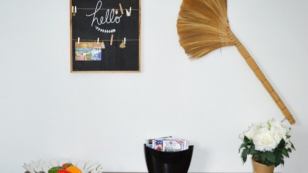 Un armario de madera con cestas de mimbre, una pizarra con 'hello' y fotografías, un ventilador y un arreglo floral blanco.