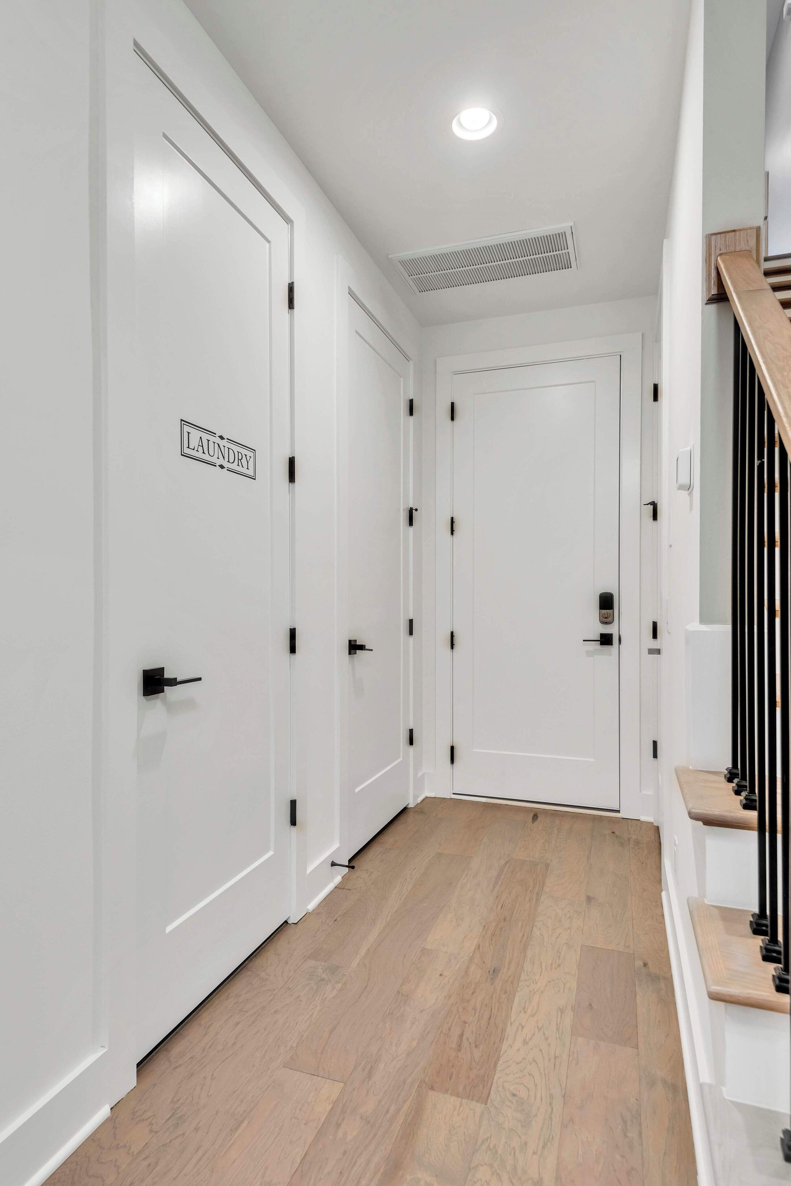 A hallway with white doors, one labeled "Laundry," and a wooden staircase on the right.