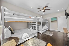 A bunk bed room with a ceiling fan, a television, and a door leading to another room.