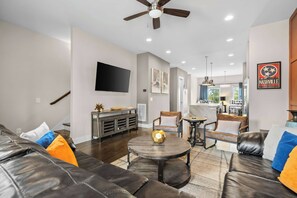 A modern living room with a leather sofa, a round coffee table, and a flat-screen TV mounted on the wall.
