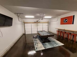 A room with a pool table, a mounted TV, and a flag on the wall. - Music City Gem | 2 Miles to Downtown | Rooftop! (Nashville)