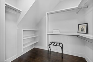 A walk-in closet with white shelving, a black metal drying rack, and a framed picture on the wall.