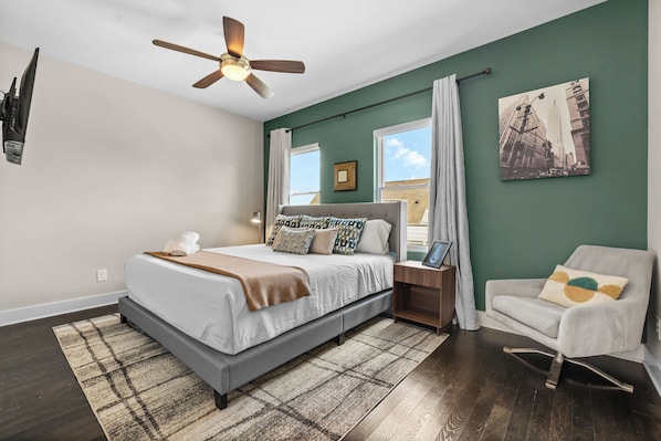 A bedroom with a bed, a chair, a nightstand, a ceiling fan, and a window.