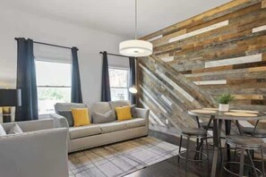 Uma sala de estar moderna com sofá, uma mesa de jantar com cadeiras, um lustre e uma parede de destaque em madeira.