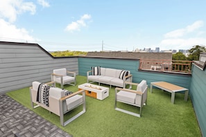 A rooftop patio with a seating area, a fire pit, and a view of the city skyline.