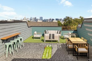 A rooftop patio with a green artificial turf, a wooden table, a sofa, and a small pool table.