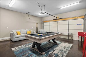 A pool table in a room with a grey sofa, a red cabinet, and a garage door.