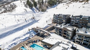 A modern hotel with a rooftop pool, ski slopes in the background, and a mountainous landscape. - Apex Ski In/Out Canyons Village Beautiful 3 Bedroom, Private Hot Tub, Community Pool (Park City)