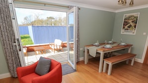 Una habitación con un sillón rojo, una mesa de comedor de madera dispuesta para cuatro personas y vistas a un jardín a través de una puerta corrediza de vidrio.
