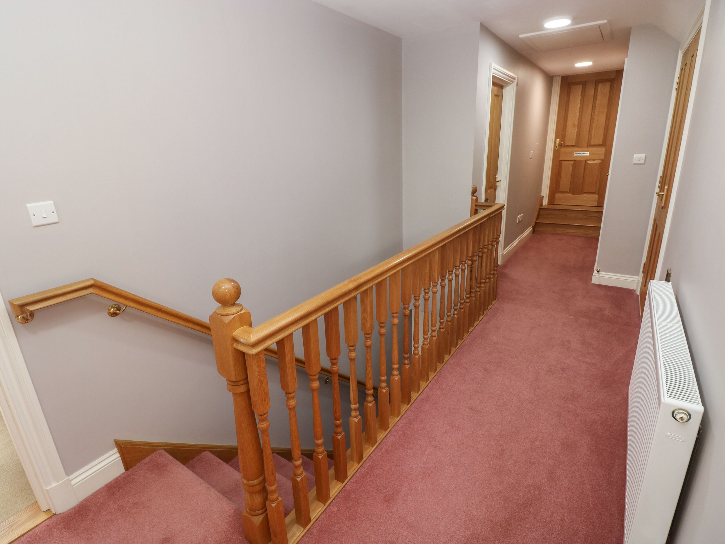 Un escalier recouvert de moquette, avec des rampes en bois et un mur blanc.