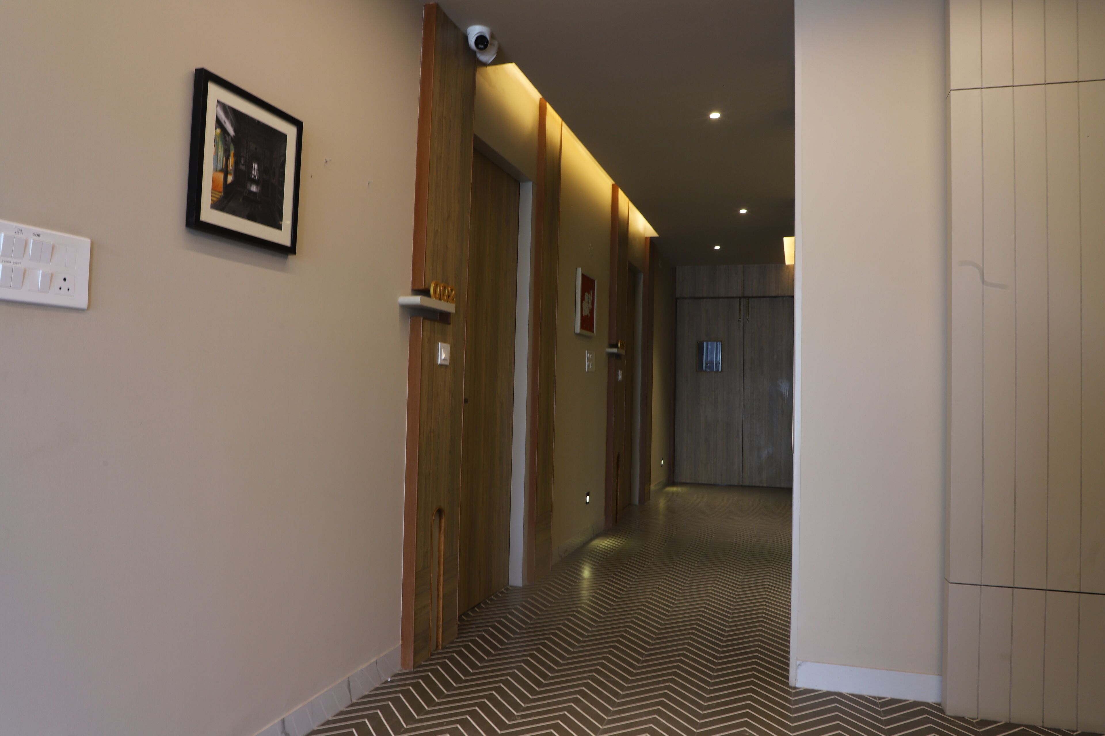 A hallway with wooden doors, a patterned floor, and a security camera on the wall.