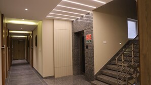 Un couloir d’hôtel avec un sol recouvert de moquette, une porte en bois, un mur en granit et un escalier doté de rampes en métal.