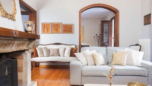 Uma sala de estar com lareira, um sofá cinza com várias almofadas e quadros nas paredes.