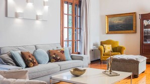 Uma sala de estar com um sofá cinzento, uma poltrona amarela, uma mesa de centro branca e um quadro na parede.