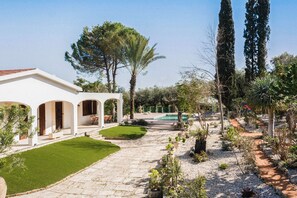 Stroll through the serene garden, featuring a variety of plants and trees, and access the welcoming entrance of this property.