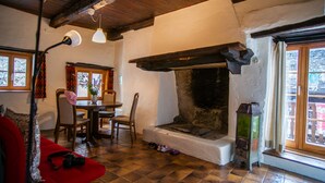 Un salon chaleureux avec une cheminée, des poutres en bois, une table à manger avec des chaises et un canapé rouge.
