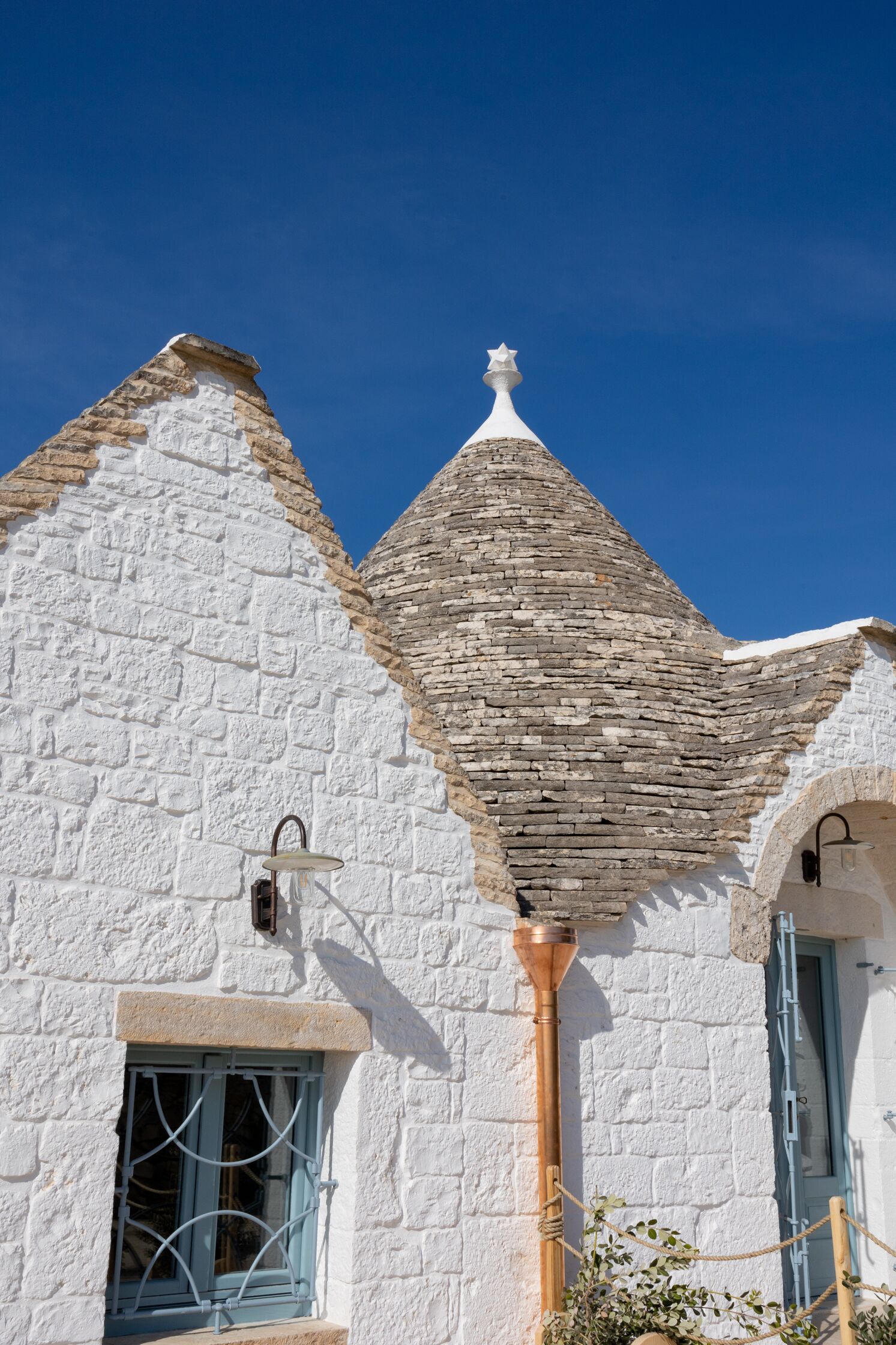 Un edificio blanco con techo de piedra y una ventana pequeña con contraventanas azules.