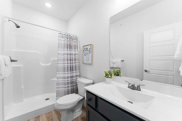 A modern bathroom with a shower, toilet, sink, and a large mirror.