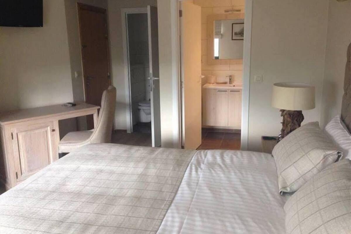 Ein Schlafzimmer mit Bett, Schreibtisch, Stuhl und angrenzendem Badezimmer, das durch eine offene Tür sichtbar ist.
