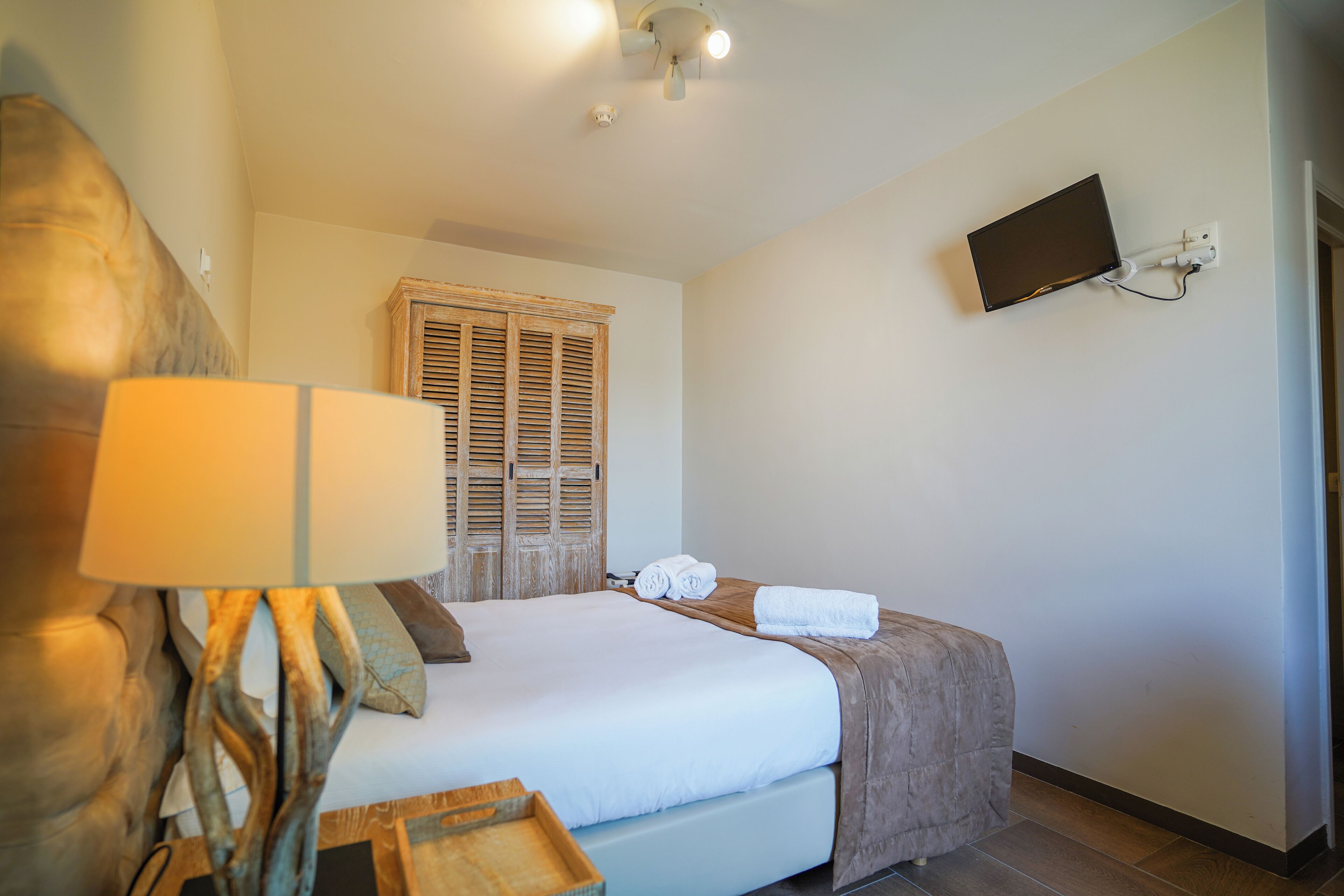Una camera d'albergo ordinata con un letto, una lampada da comodino, una televisione montata a parete e una porta in legno.