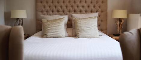 A neatly made bed with a tufted headboard, two bedside lamps, and a wooden nightstand.
