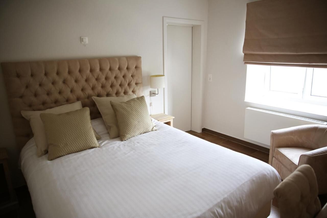 A neatly made bed with a tufted headboard, a bedside lamp, and a chair to the right.