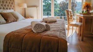 Una cama bien tendida con un edredón marrón, una toalla enrollada y una silla con una mesita de madera al lado.