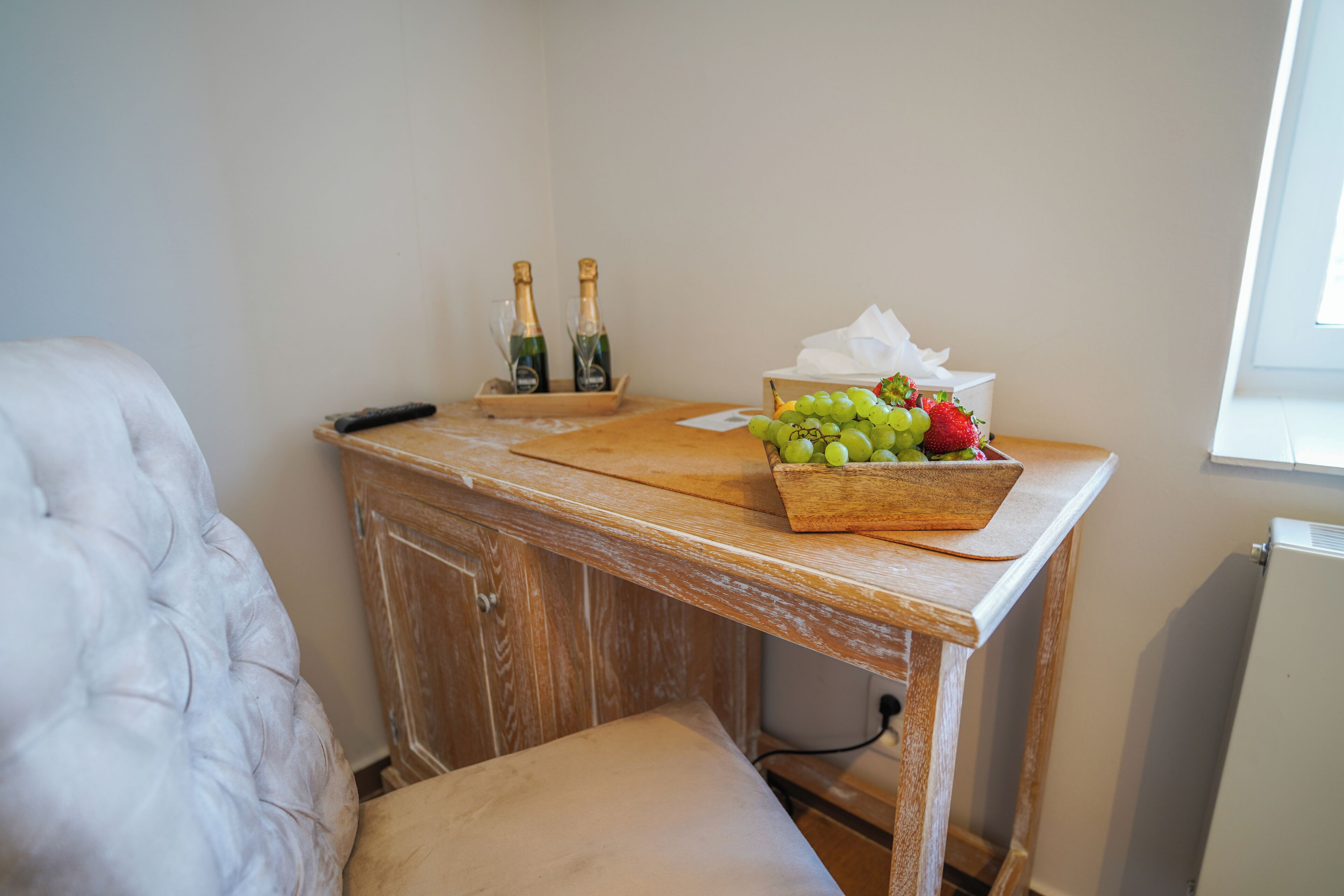 A wooden table with a box of grapes, two bottles of champagne, and a remote control.