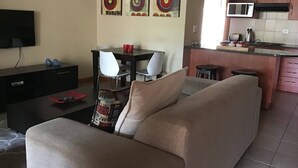 Un salon comprenant un canapé, un téléviseur, une table à manger avec des chaises et un coin cuisine équipé d’un four à micro-ondes.