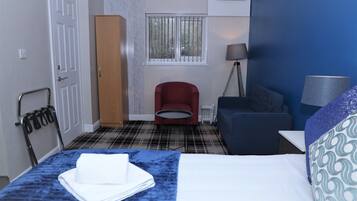A hotel room with a bed, a red chair, a blue sofa, a lamp, and a window with bars.