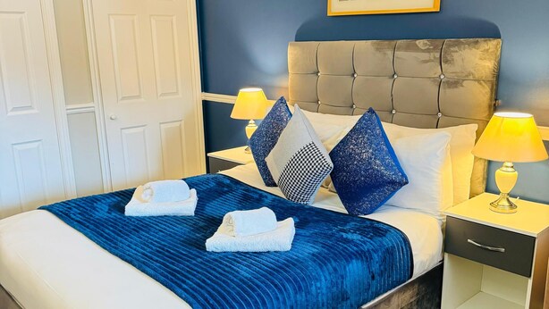 Habitación de hotel con cama, dos mesitas de noche, una lámpara, un marco de fotos y una puerta.