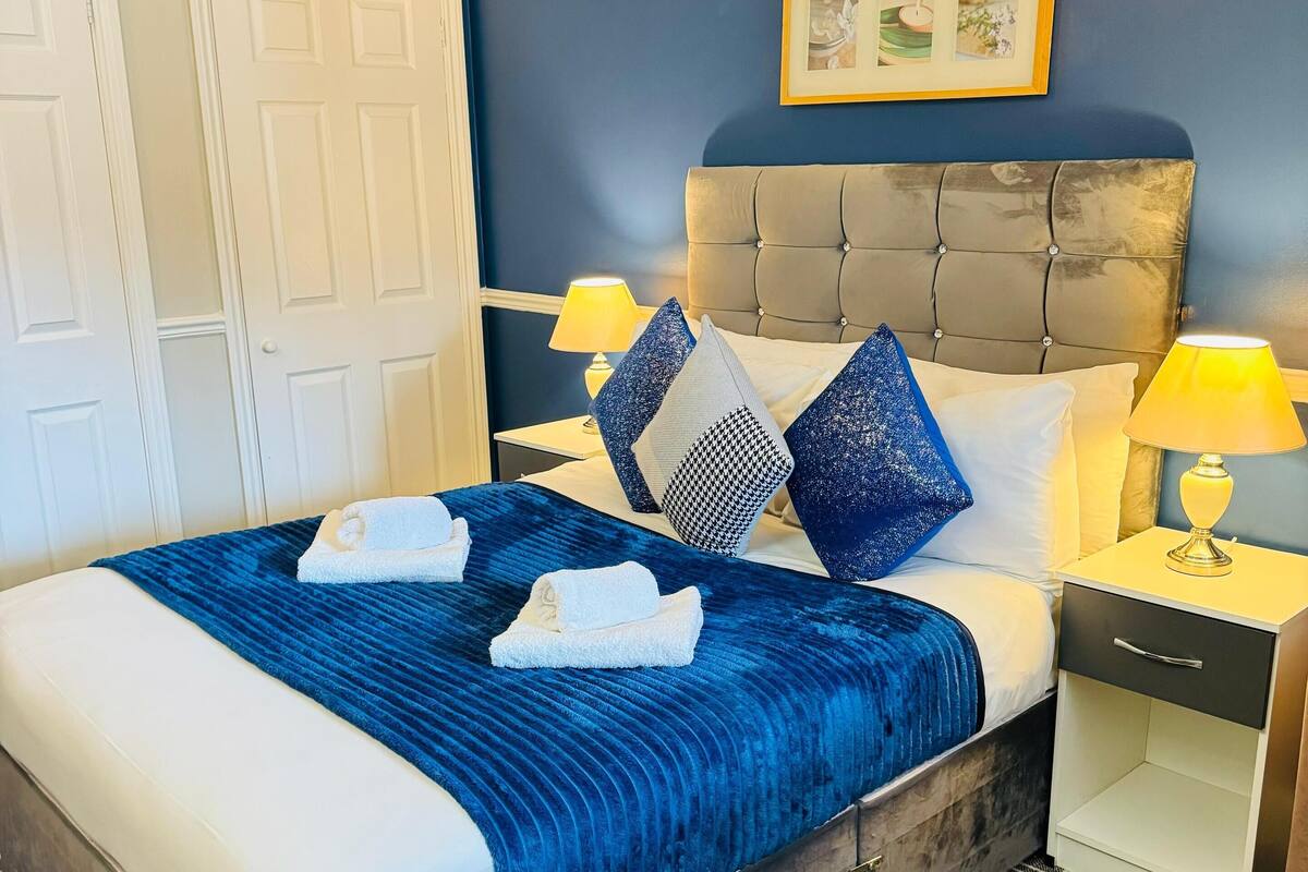 Habitación de hotel con cama, dos mesitas de noche, una lámpara, un marco de fotos y una puerta.