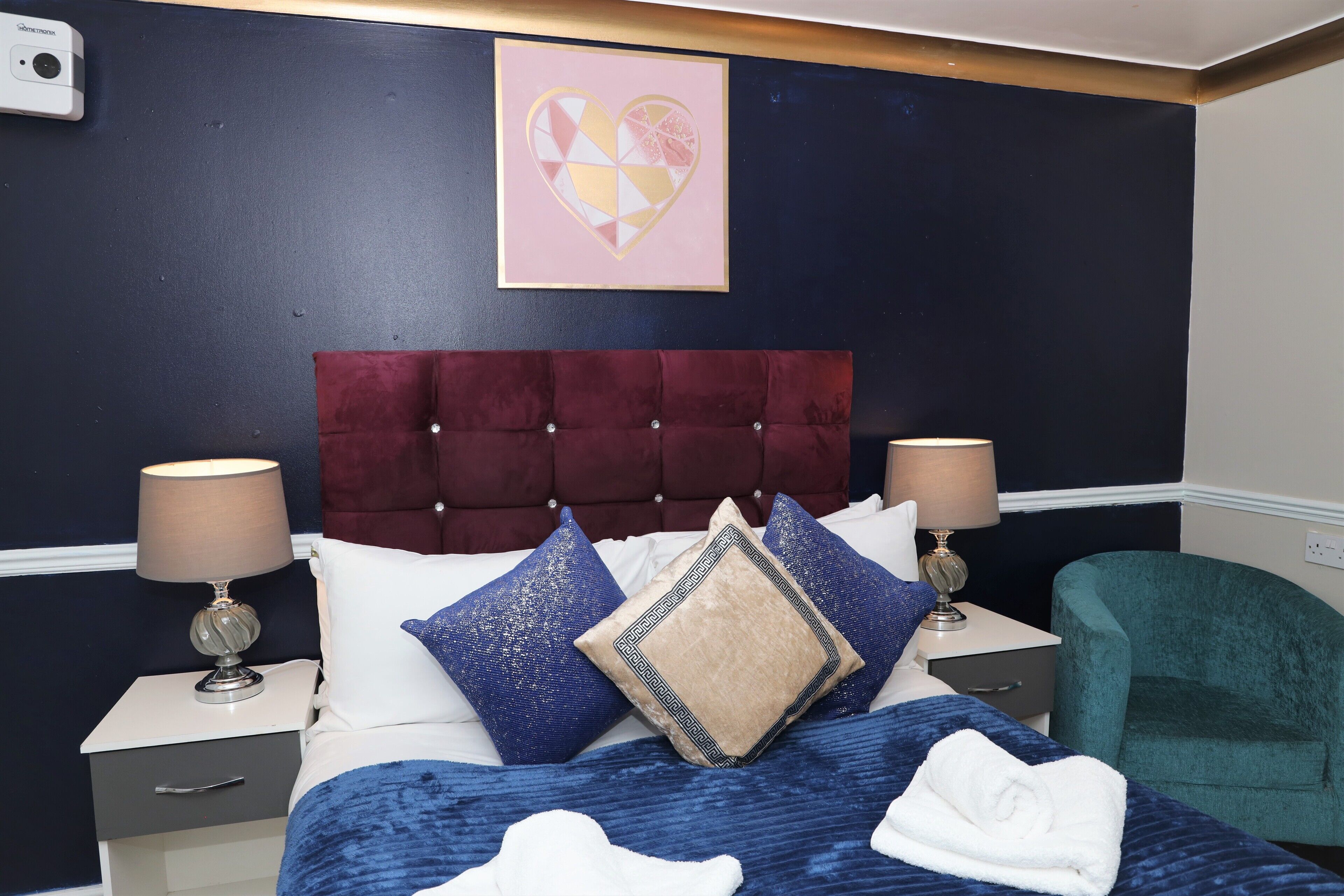 A neatly made bed with a tufted headboard, two bedside tables with lamps, and a teal armchair.
