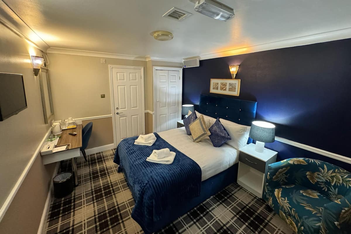 Habitación de hotel con cama, escritorio, silla, cesto de basura y lámpara fijada a la pared.