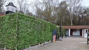 Un edificio con un acceso cubierto, un cartel y un muro de jardín con plantas trepadoras.