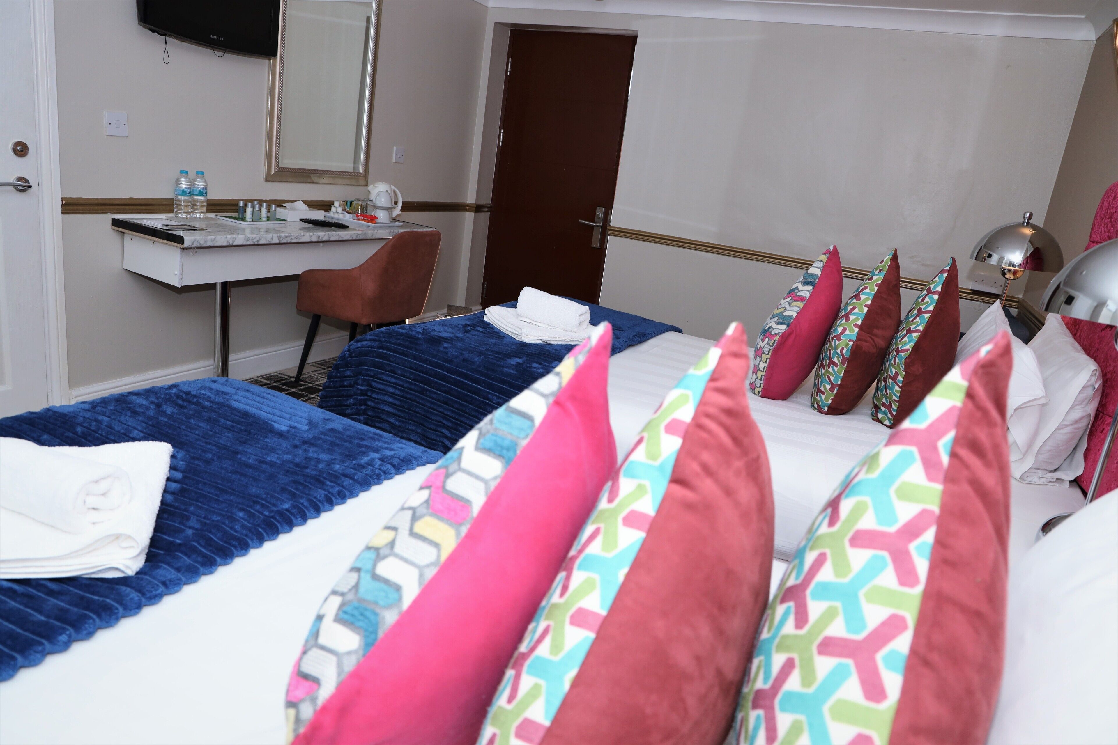 Une chambre d’hôtel avec deux lits, un bureau, une chaise, une télévision et une porte.