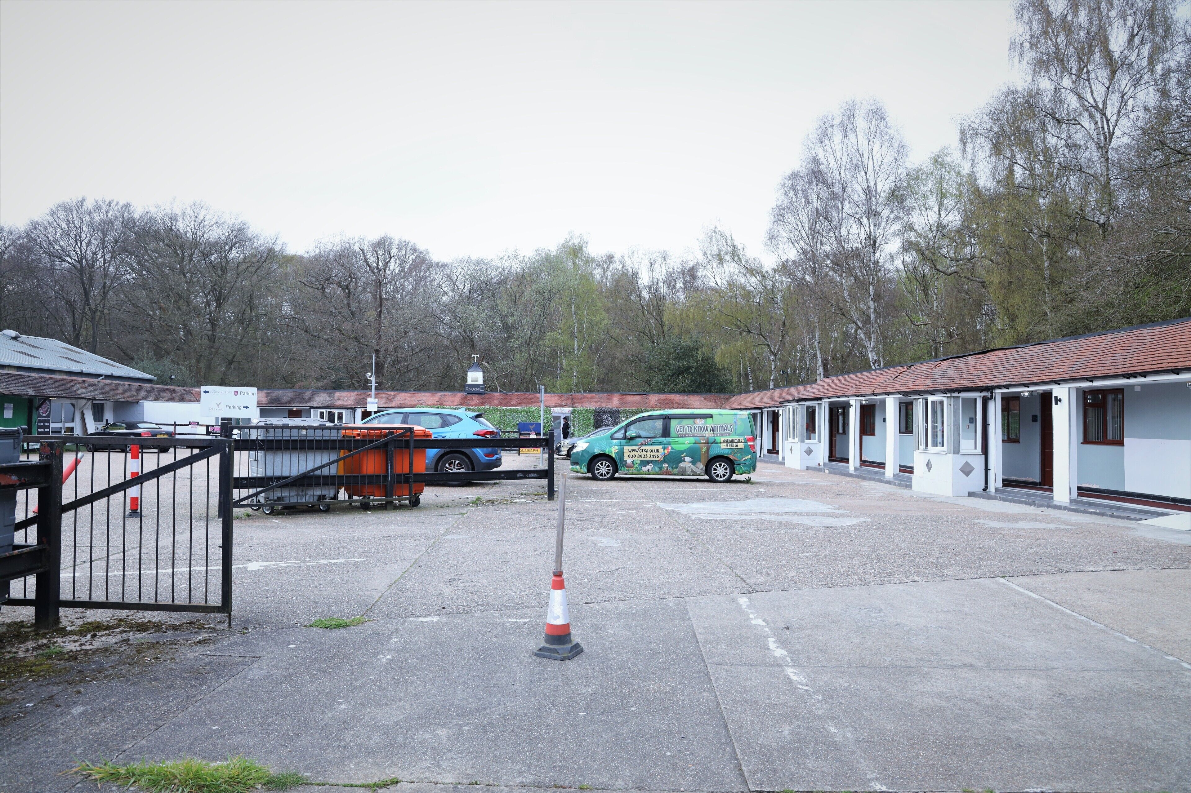 A motel with a parking area, a green van, and a gated entrance.