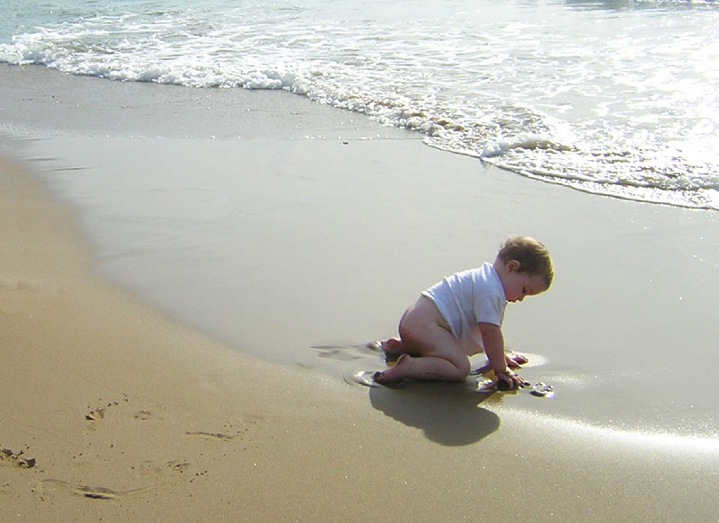 Een kind speelt op een zandstrand met zachte golven.