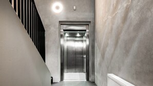 A modern elevator in a hallway with a concrete wall and a metal staircase to the left.