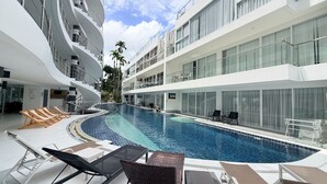 Ein modernes Hotel mit Schwimmbad, Liegestühlen und einem mehrstöckigen Balkon.