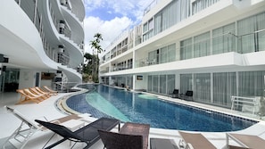 Un hotel moderno con piscina, sdraio e un balcone a più livelli.