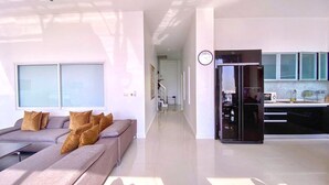 Ein modernes Wohnzimmer mit Sofa, einer Küchenzeile inklusive Kühlschrank und einem Flur.