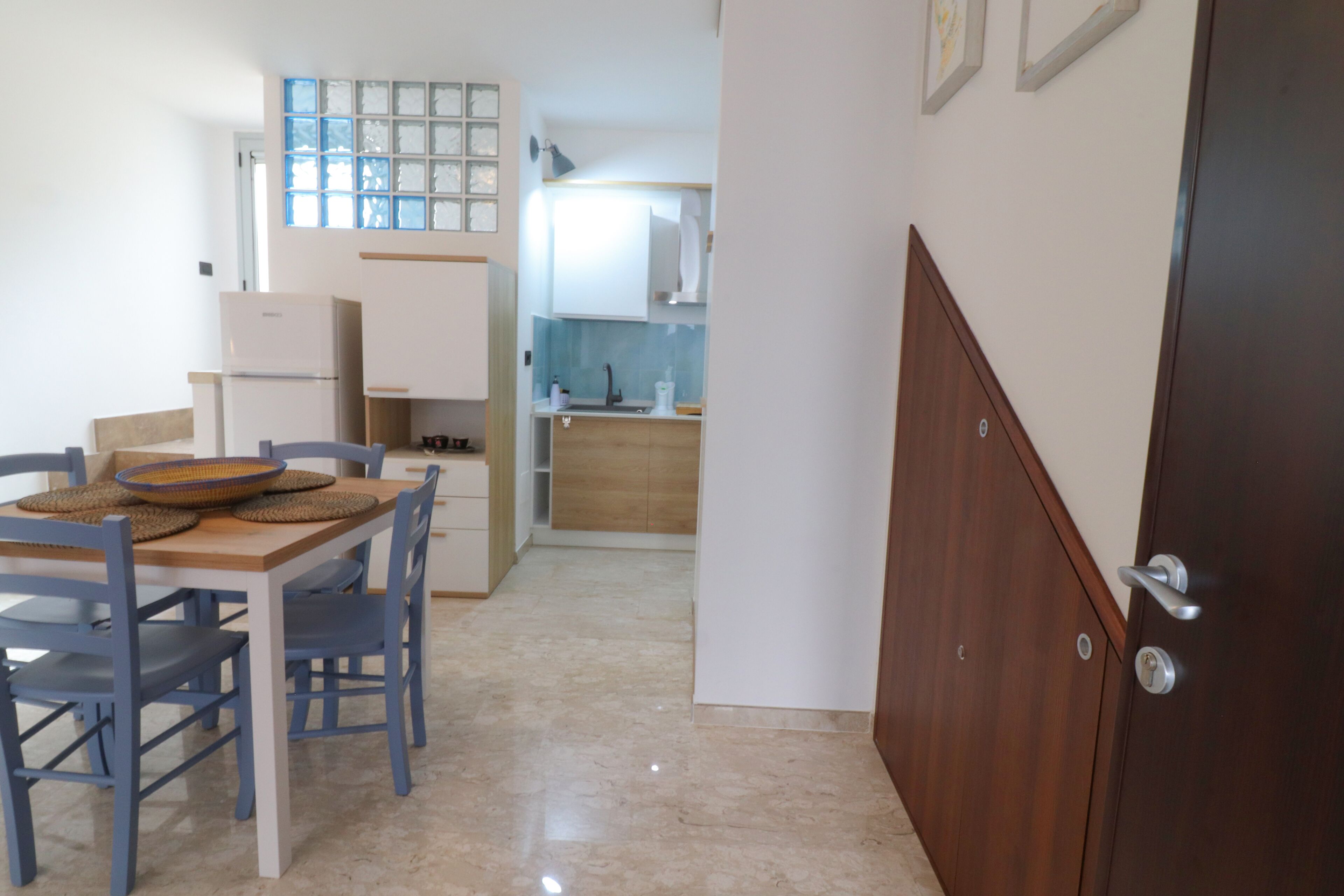 Eine kleine Küche mit Kühlschrank, Spüle und Holzschränken. Ein Essbereich mit Tisch und Stühlen ist ebenfalls vorhanden.