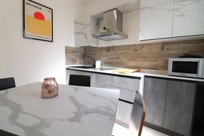 Une cuisine moderne avec un plan de travail en marbre, une hotte en acier inoxydable, un four à micro-ondes et un tableau encadré au mur.