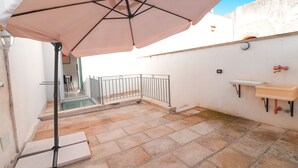 Ein Patio mit Fliesenboden, Metallgeländer, einem Waschbecken und einem großen Sonnenschirm.