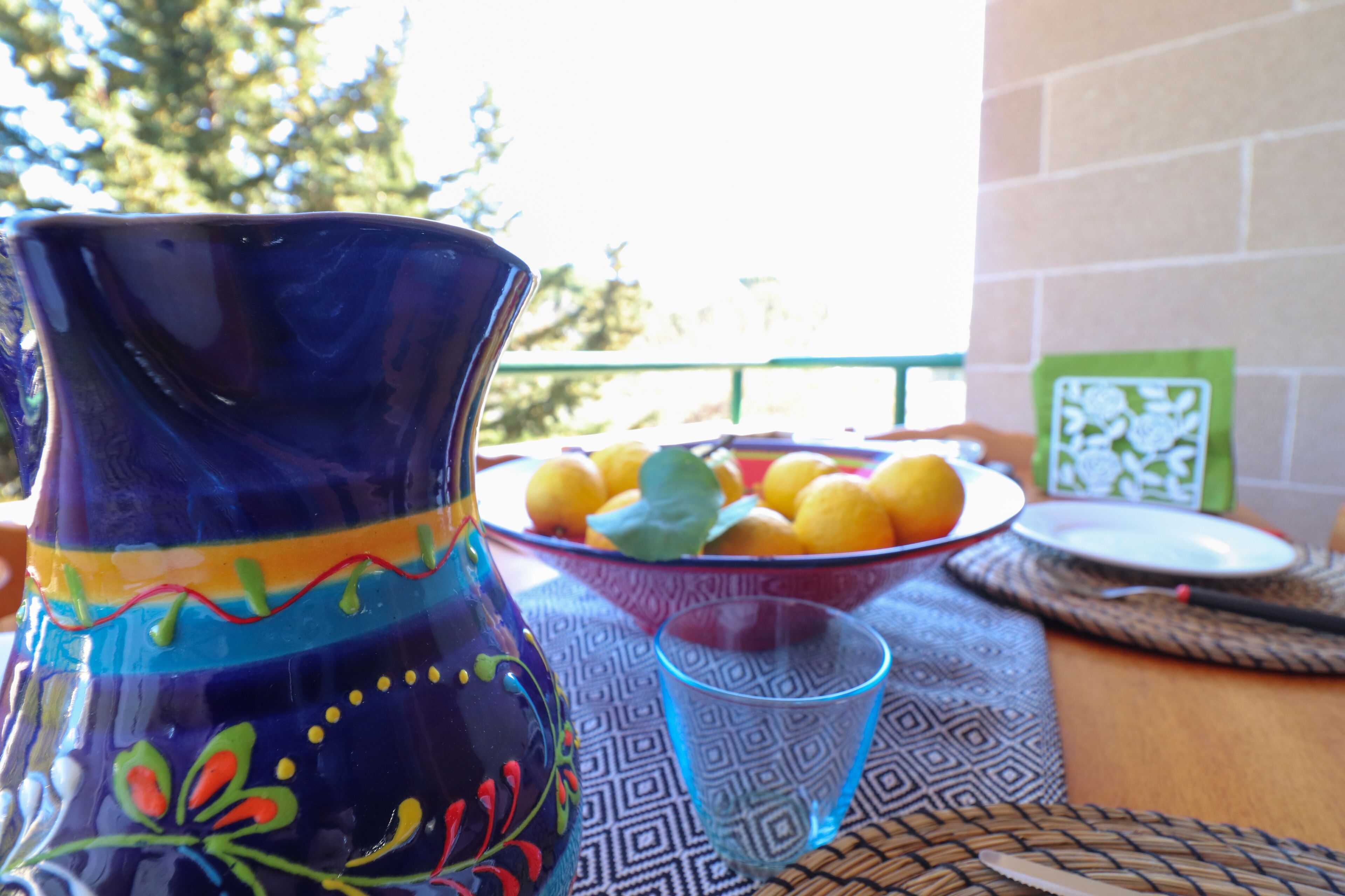 A table with a decorative vase, a bowl of fruit, and a glass.