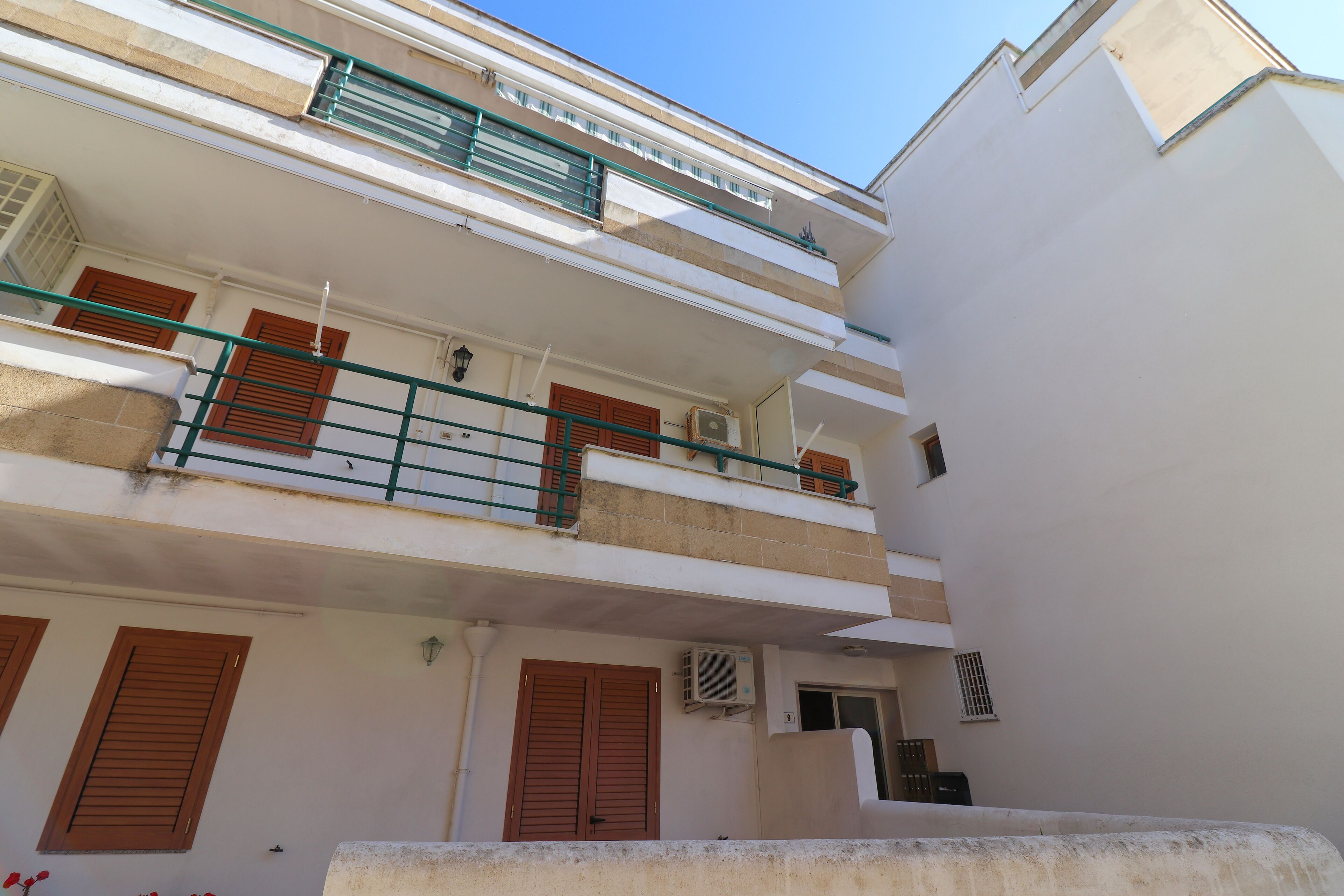 Un edificio de varios pisos con balcones, ventanas con contraventanas y un equipo de aire acondicionado.