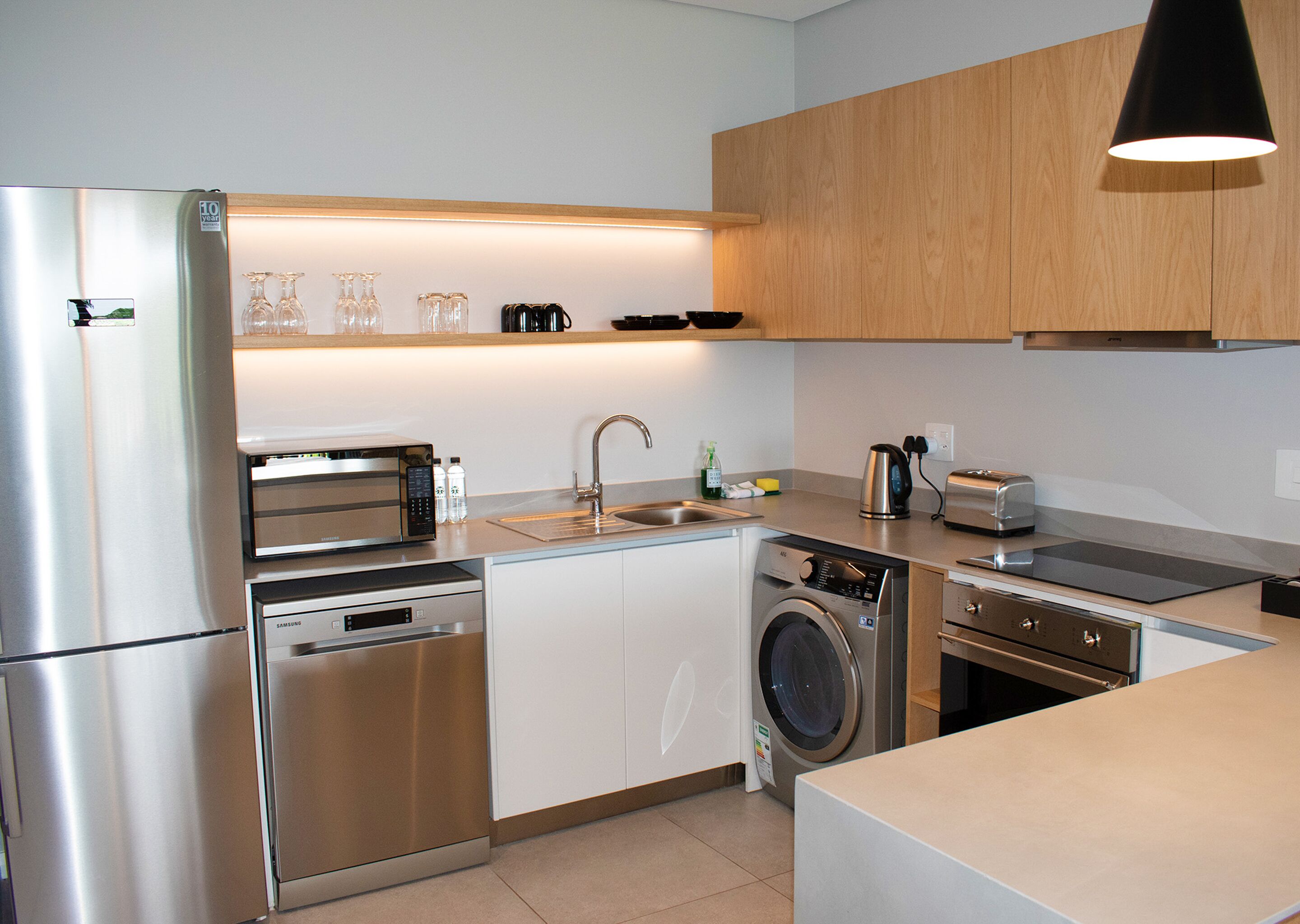 A modern kitchen with stainless steel appliances, a dishwasher, a washing machine, and wooden cabinets.