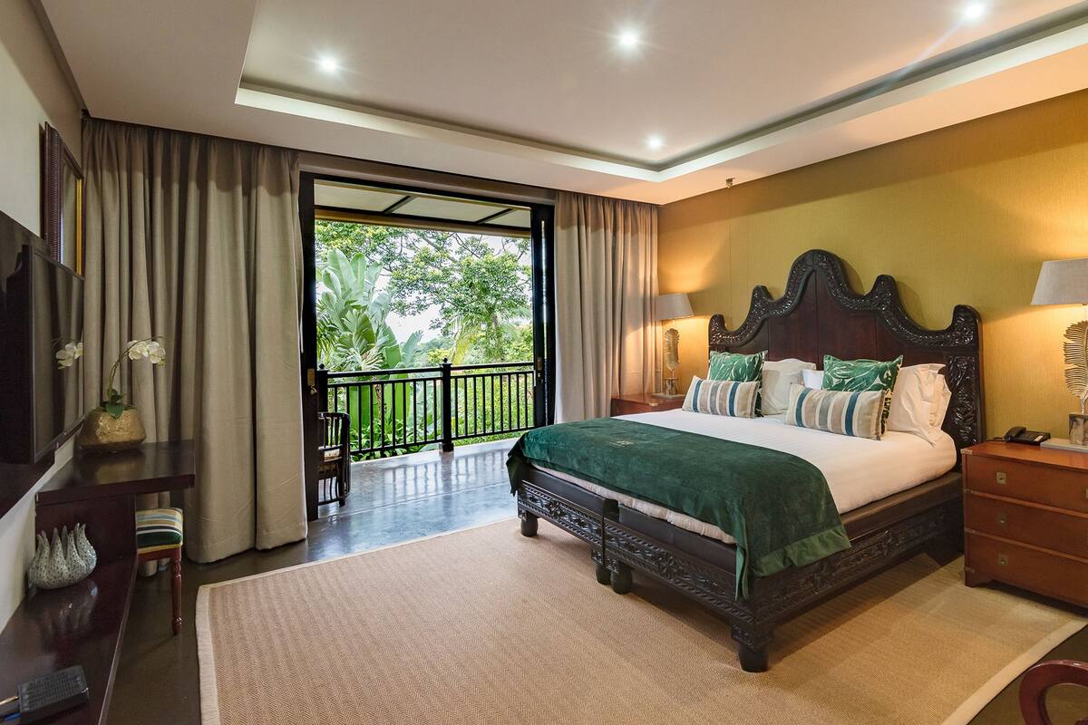 Une chambre spacieuse avec un grand lit, un balcon et une vue sur la verdure.
